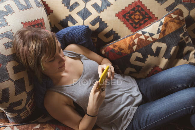 Femme utilisant un téléphone portable tout en étant couché sur le canapé dans le salon — Photo de stock