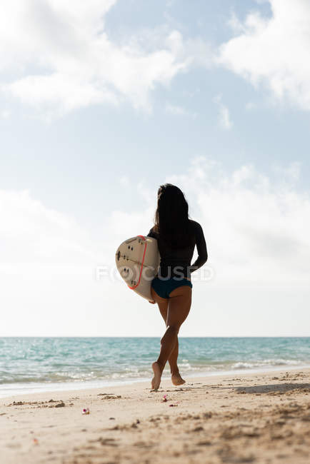 Жінка біжить з дошкою для серфінгу на пляжі в сонячний день — стокове фото