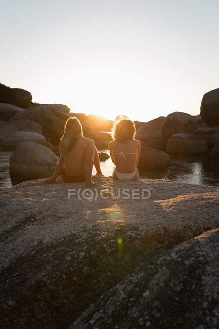 Vista trasera de la pareja sentados juntos en una roca en la playa - foto de stock
