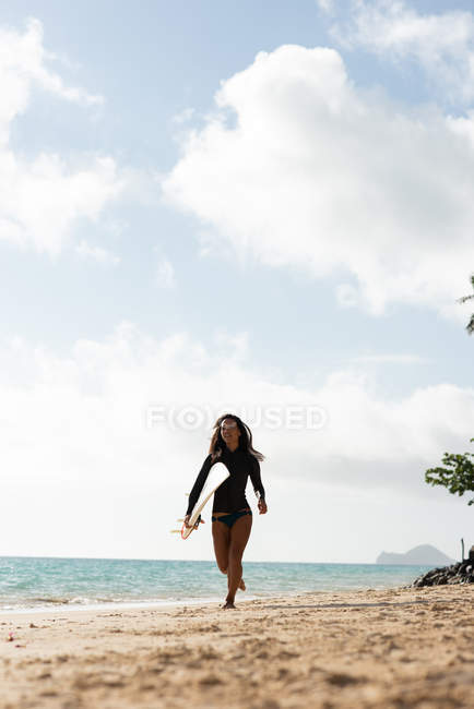 Donna che corre con la tavola da surf in spiaggia in una giornata di sole — Foto stock
