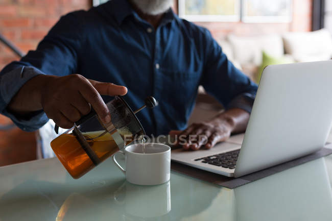 Senior gießt Kaffee ein, während er zu Hause Laptop benutzt — Stockfoto