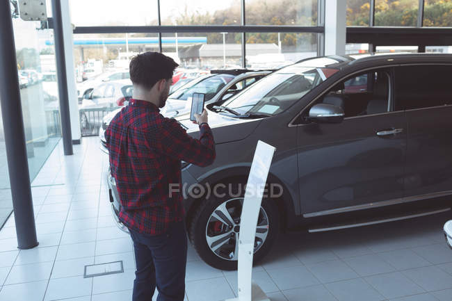 Vendedor tirando foto de carro com telefone celular no showroom — Fotografia de Stock