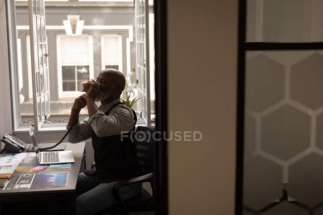 Senior graphic designer talking on landline at desk in office — Stock Photo
