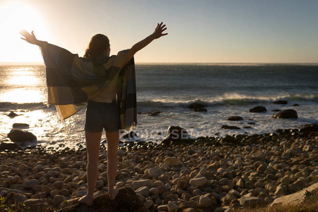 Жінка з простягнутими руками стоїть на скелі на заході сонця — стокове фото