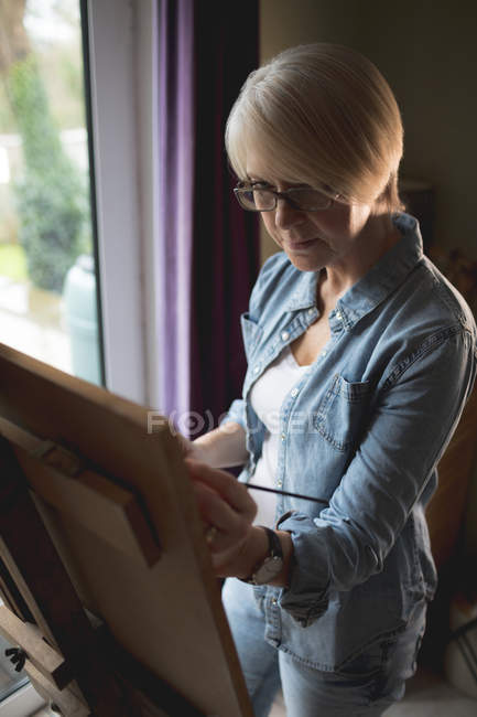 Female artist painting on a canvas with a paintbrush at home — Stock Photo