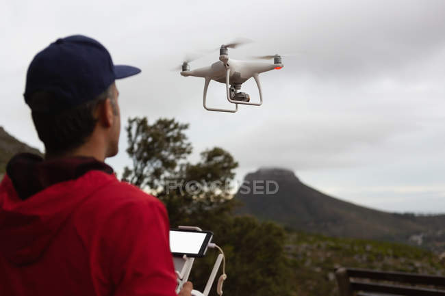 Vista trasera del hombre operando un avión no tripulado volador en el campo - foto de stock