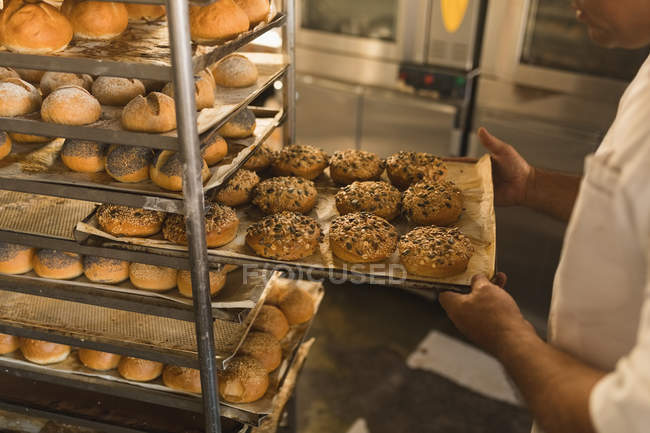 Panadero masculino quitando una bandeja de alimentos dulces en la panadería - foto de stock