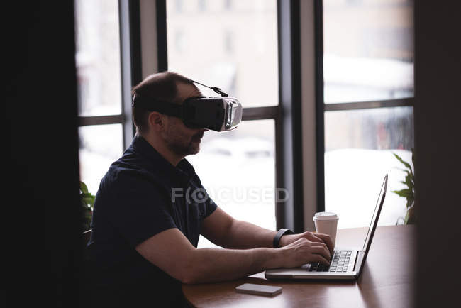 Чоловік виконавчий використовує гарнітуру віртуальної реальності з ноутбуком за столом в офісі — стокове фото