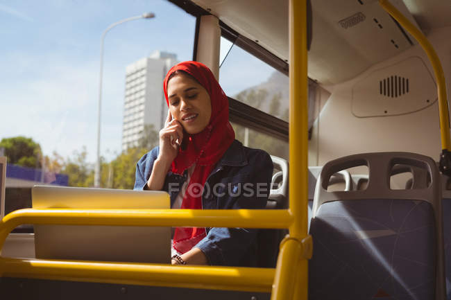 Bella donna hijab con computer portatile che parla sul telefono cellulare in autobus — Foto stock