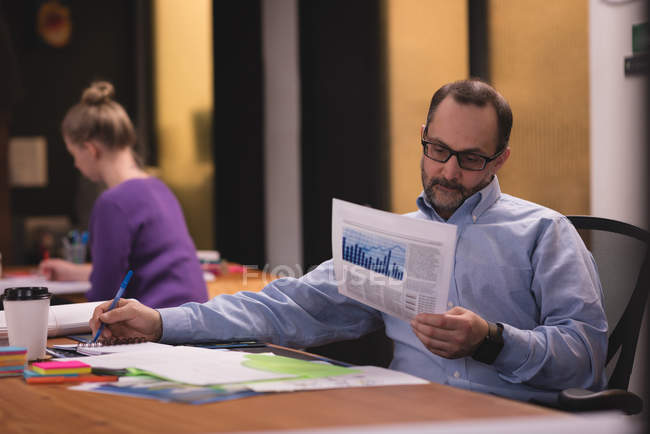 Executivo masculino olhando para o documento gráfico no escritório — Fotografia de Stock