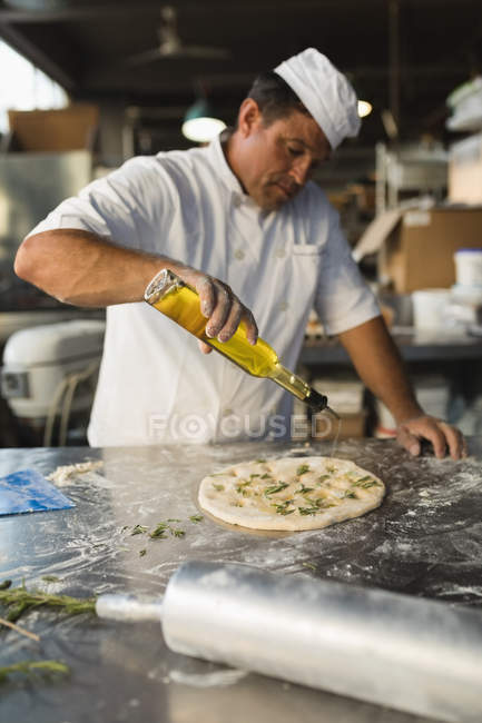 Cocinero macho vertiendo aceite sobre una masa en una panadería - foto de stock