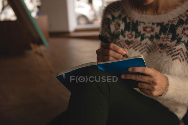 Mid section of businesswoman writing on a book in cafeteria at office — Stock Photo