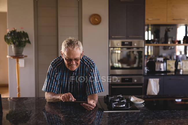 Старший чоловік використовує цифровий планшет на кухні вдома — стокове фото