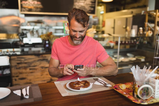 Усміхнений чоловік використовує мобільний телефон у хлібопекарні — стокове фото