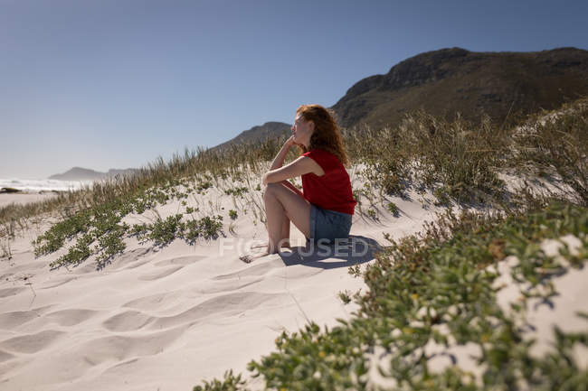 Vista lateral da mulher sentada na areia na praia em um dia ensolarado — Fotografia de Stock