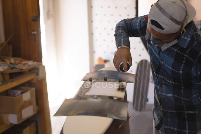 Man spray painting skateboard in workshop — Stock Photo