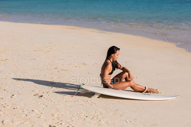 Женщина отдыхает с доской для серфинга на пляже в солнечный день — стоковое фото
