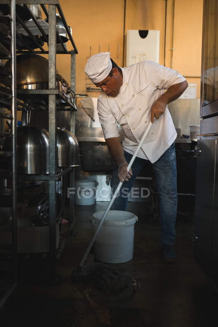 Male baker cleaning floor with floor mop in bakery shop — Stock Photo