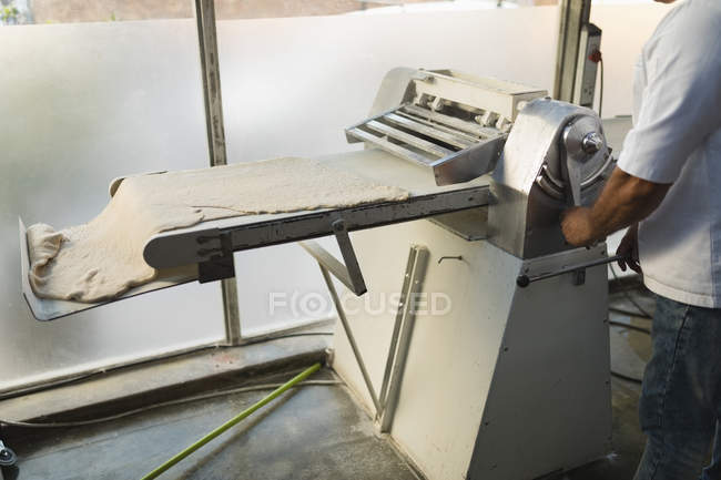 Sección media del panadero masculino utilizando la máquina en la panadería - foto de stock