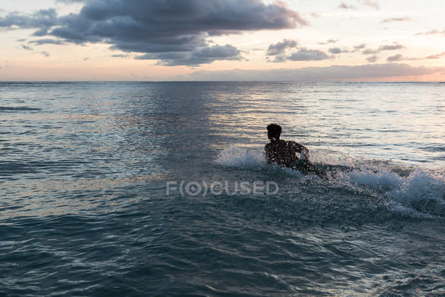 Surfer surft mit Surfbrett in der Abenddämmerung im Meer — Stockfoto