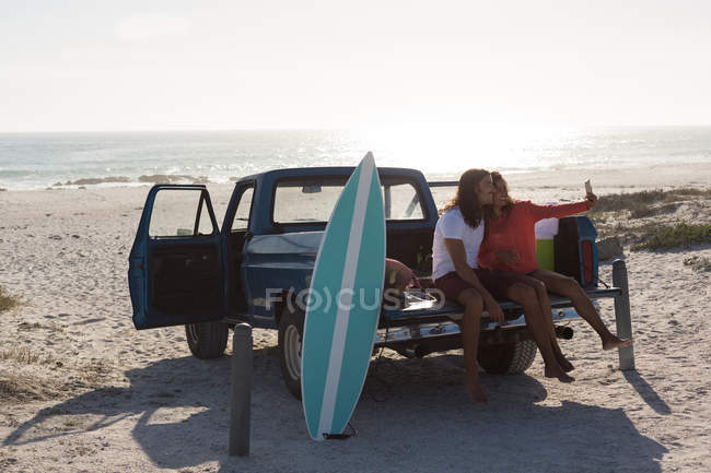 Casal tirando selfie com telefone celular em um caminhão de coleta na praia — Fotografia de Stock