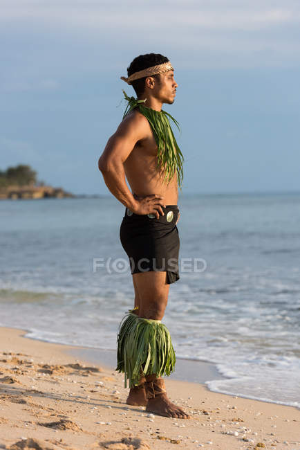 Задумчивый танцор огня стоя с руками на бедре на пляже — стоковое фото