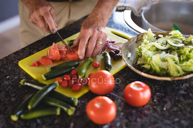 Средняя часть пожилого человека режет овощи на кухне дома — стоковое фото