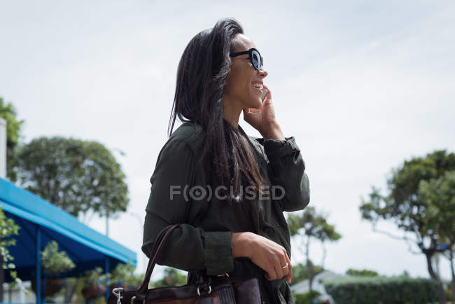 Усміхнена жінка в сонцезахисних окулярах говорить на мобільному телефоні — стокове фото