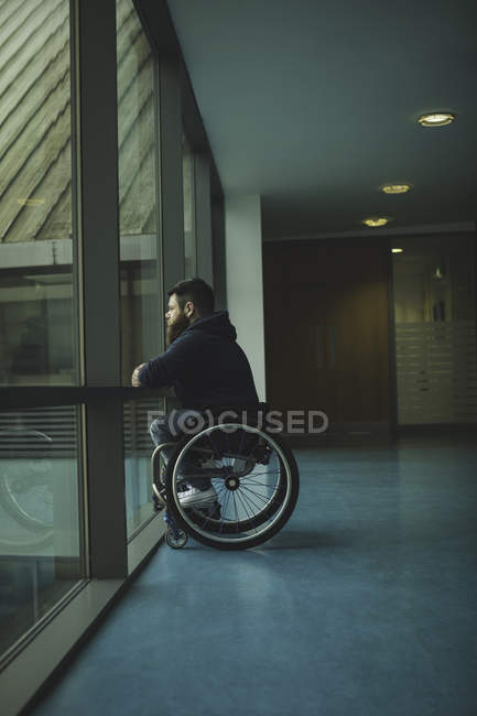 Вид збоку інваліда на інвалідному візку, який дивиться зі скляної панелі — стокове фото