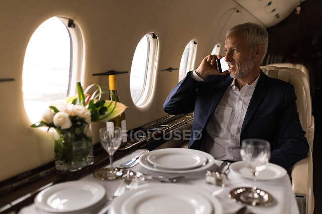 Старший бизнесмен разговаривает по мобильному телефону в частном самолете — стоковое фото