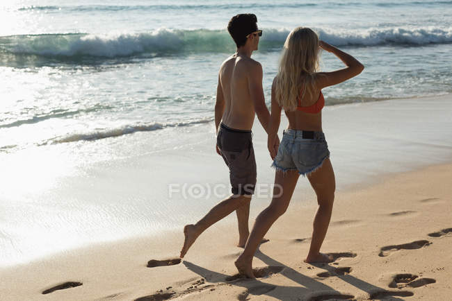 Пара, идущая вместе рука об руку на пляже — стоковое фото
