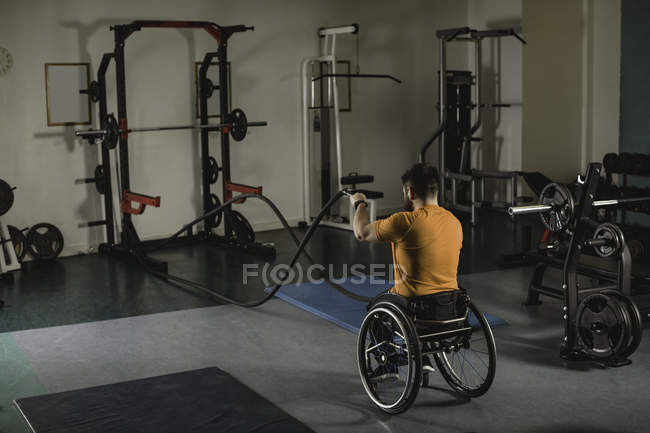 Gehbehinderter Mann im Rollstuhl trainiert mit Kampfseilen in Turnhalle — Stockfoto