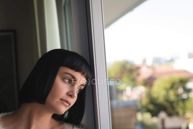 Продумана жінка дивиться крізь вікно вдома — стокове фото