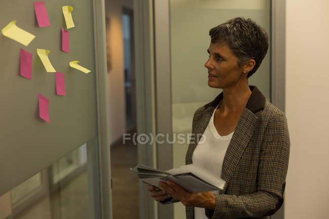Donna d'affari matura in cerca di appunti appiccicosi sul muro in ufficio — Foto stock