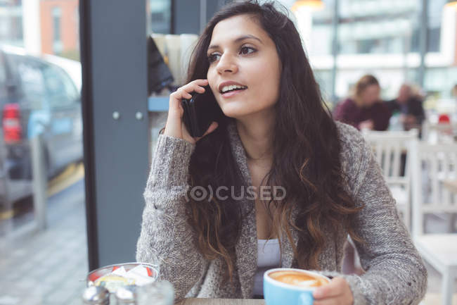 Woman talking on mobile phone while having coffee in coffee shop — Stock Photo