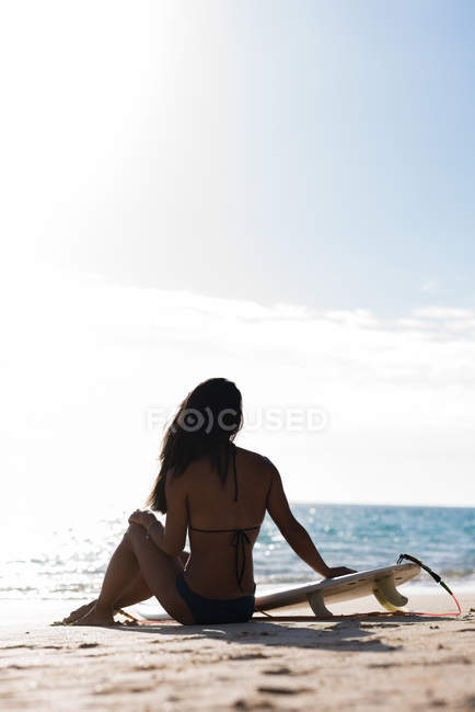 Вид ззаду жінки, що розслабляється з дошкою для серфінгу на пляжі — стокове фото