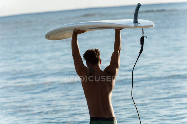 Vista trasera del surfista masculino caminando con tabla de surf en la playa - foto de stock