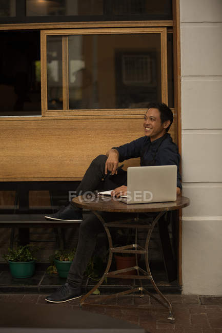 Empresário sorridente com laptop sentado no café pavimento — Fotografia de Stock