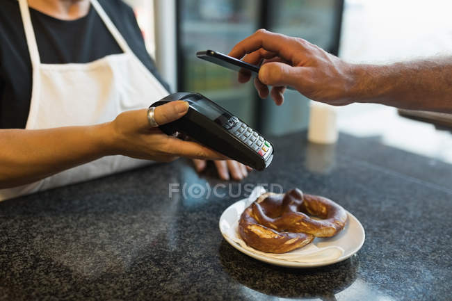Cliente haciendo el pago a través del teléfono móvil en panadería - foto de stock
