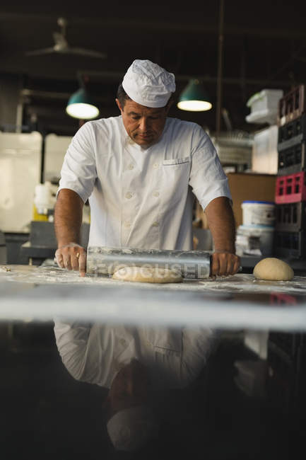 Mature male baker using rolling pin in bakery shop — Stock Photo