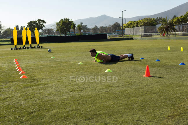 Jugador haciendo push up en el campo en un día soleado - foto de stock