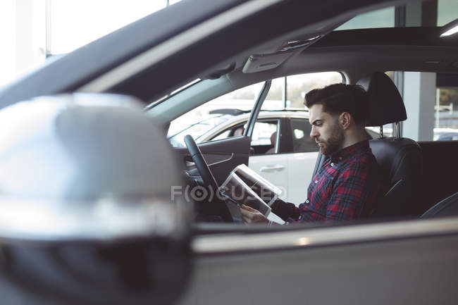 Vendeur lisant la brochure à l'intérieur de la voiture au showroom — Photo de stock