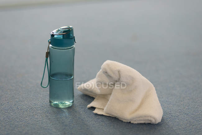 Close-up of water sipper with towel at fitness studio — Stock Photo
