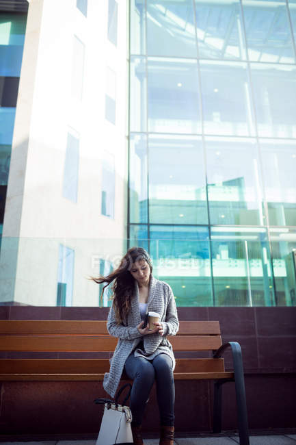 Mujer joven sosteniendo una taza de café desechable en la ciudad - foto de stock