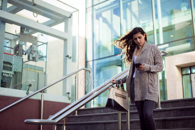 Young woman using mobile phone while walking downstairs in the city — Stock Photo