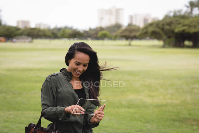 Femme souriante utilisant une tablette numérique en verre dans le parc — Photo de stock
