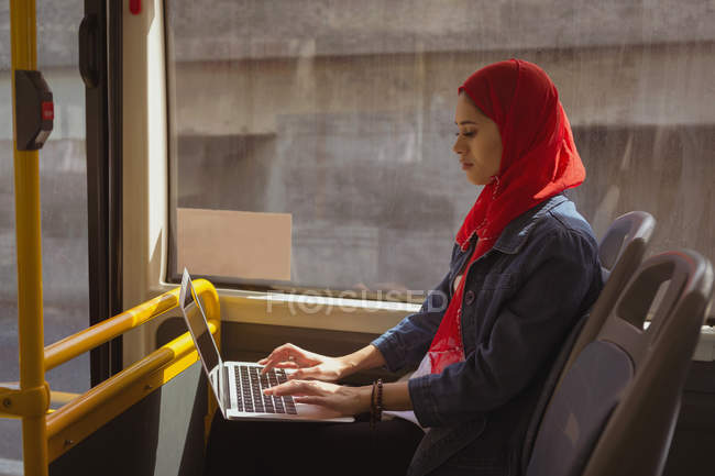 Hermosa mujer hijab utilizando el ordenador portátil mientras viaja en autobús - foto de stock