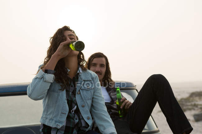 Casal tomando cerveja em um capô de caminhão de coleta na praia — Fotografia de Stock