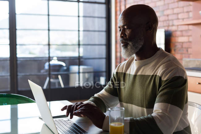 Senior man sitting on table while using laptop at home — Stock Photo