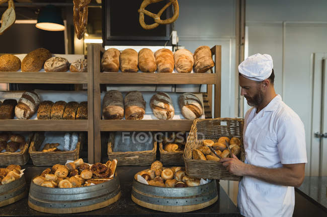 Male baker holding basket of croissants in bakery shop — Stock Photo
